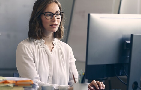 A woman wearing glasses views a monitor screen.